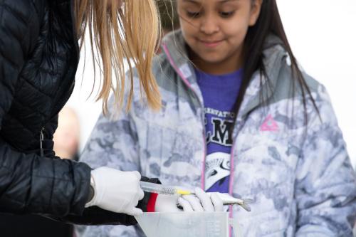 A student watches as a researcher holds a juvenile salmon and tags it with a passive acoustic transmitter.
